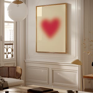 May include: A framed print of a blurred pink heart on a cream background. The frame is gold and the heart is centered in the image.