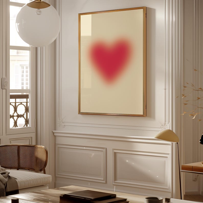 May include: A framed print of a blurred pink heart on a cream background. The frame is gold and the heart is centered in the image.