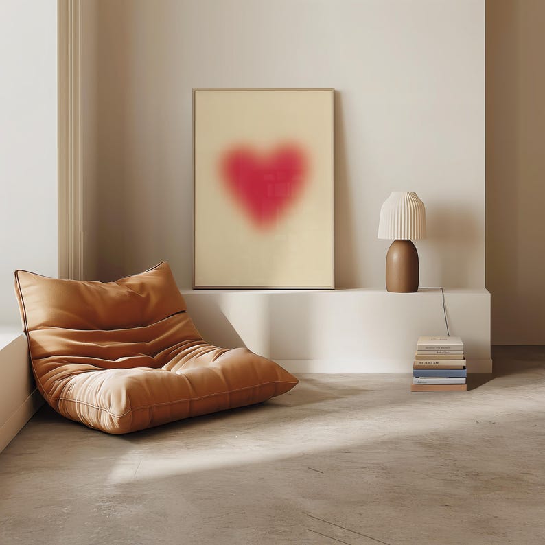 May include: A brown leather armchair with a white wall and a framed print of a pink heart shape in the background. A white lamp with a brown base sits on a white shelf.