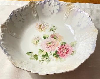 May include: A white ceramic serving bowl with a scalloped edge and floral design. The bowl features a central cluster of pink and white chrysanthemums with green leaves. The rim has a subtle iridescent sheen and embossed floral accents.