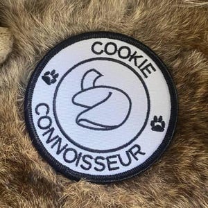 May include: Black and white embroidered patch with the text "COOKIE CONNOISSEUR" in a circle. A fortune cookie is in the center of the circle.