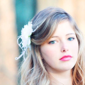K&ouml;nnte beinhalten: Eine junge Frau mit langen blonden Haaren, die mit einer wei&szlig;en Blume hinter dem Ohr gestylt sind. Sie tr&auml;gt leichtes Make-up und hat einen sanften, nat&uuml;rlichen Look.