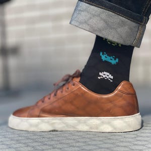Peut inclure: Baskets basses en cuir marron avec semelles blanches et chaussettes noires à motif de vaisseaux spatiaux pixelisés.