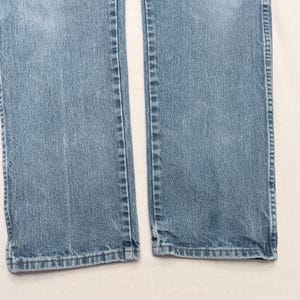 May include: Light blue denim jeans. The image shows the lower portion of the jeans, with the legs separated. The denim has a classic, faded look, with visible seams and a slightly worn appearance. The hem is visible at the bottom.