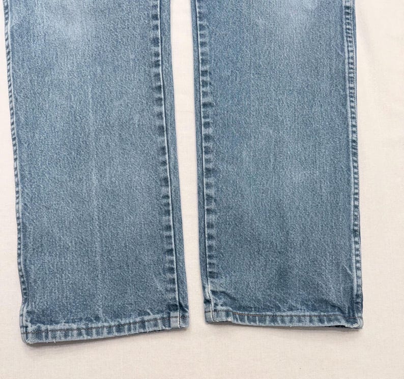 May include: Light blue denim jeans. The image shows the lower portion of the jeans, with the legs separated. The denim has a classic, faded look, with visible seams and a slightly worn appearance. The hem is visible at the bottom.