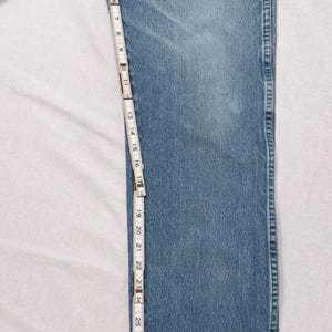 May include: Light blue denim jeans with a straight leg, measured with a ruler. The jeans are approximately 32 inches long. The ruler shows measurements in inches and has the text "JDV Equipment Corporation".