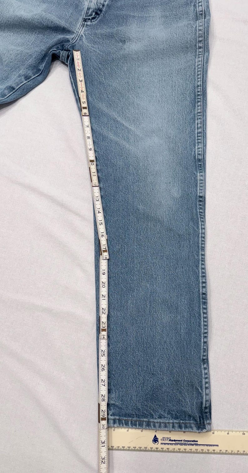 May include: Light blue denim jeans with a straight leg, measured with a ruler. The jeans are approximately 32 inches long. The ruler shows measurements in inches and has the text "JDV Equipment Corporation".