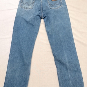 May include: Light blue denim jeans with a classic five-pocket design. The jeans feature a brown leather patch with the brand name on the back pocket. The jeans have a straight leg cut.