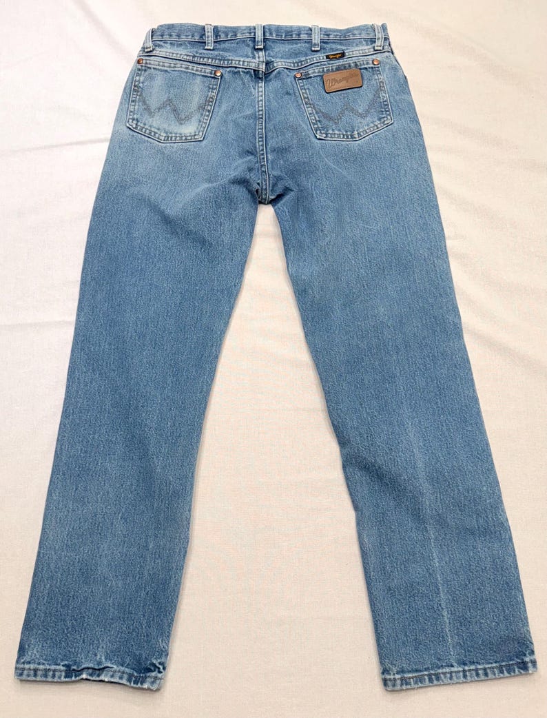 May include: Light blue denim jeans with a classic five-pocket design. The jeans feature a brown leather patch with the brand name on the back pocket. The jeans have a straight leg cut.