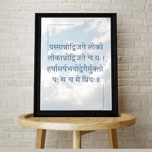 May include: A framed print with a black frame, displaying text in a script font against a cloudy sky background. The print is displayed on a light brown wooden table with a white brick wall in the background.