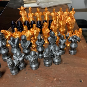 May include: A set of 32 chess pieces, 16 gold and 16 gray, with intricate designs. The pieces are arranged on a wooden surface.
