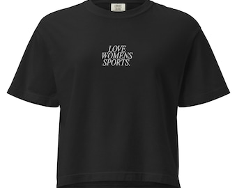 May include: Black short-sleeved t-shirt with the text "LOVE WOMENS SPORTS." in white, centered on the chest. The shirt has a crew neck and a slightly oversized fit. A small tag is visible near the neckline.