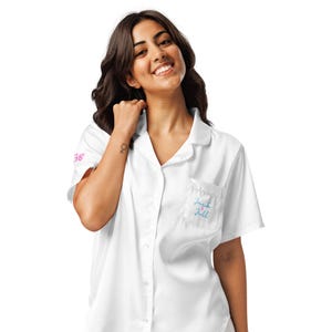 May include: White short-sleeved pajama shirt with a notched collar and a chest pocket. The shirt has the text "Jack + Jill" embroidered in blue on the pocket. The number "38" is printed in pink on the sleeve.