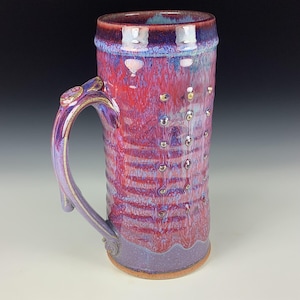 Puede incluir: Una taza de cerámica blanca con asa negra y el texto "But First, Coffee" en negrita negra. La taza se encuentra sobre un fondo borroso, sugiriendo un ambiente acogedor.