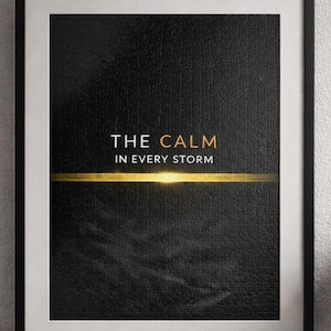 Puede incluir: Impresión artística enmarcada con el texto "THE CALM IN EVERY STORM" en letras doradas sobre un fondo negro. Una línea horizontal dorada divide el texto. La impresión está en un marco negro con un borde blanco. También se ven una pequeña planta, libros y una lámpara.