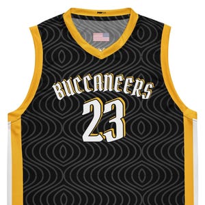 May include: Black and gold basketball jersey with the word "Buccaneers" and the number "23" in white. The jersey has a repeating pattern and an American flag on the neckline.