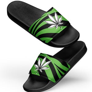 Op de afbeelding: Een paar zwarte slippers met een groen-zwart zebraprint en een wit marihuanabladontwerp.