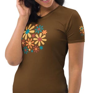 Op de afbeelding: Een bruin T-shirt met een retro bloemenontwerp in tinten oranje, geel, blauw en bruin. De bloemen zijn gestileerd en hebben een jaren '70-sfeer.