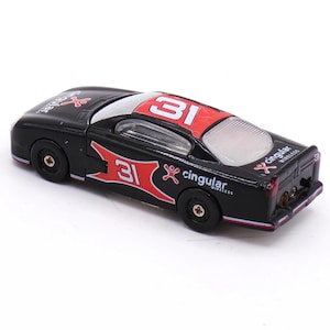 May include: A black toy race car with red and white accents. The car features the number 31 on the roof and sides, along with the "cingular wireless" logo. The car has black wheels and a clear rear window.