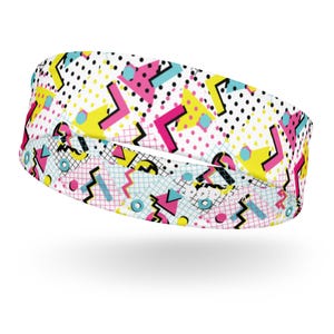 May include: A white headband with a geometric pattern in pink, yellow, and blue. The pattern includes triangles, squares, and zigzags.