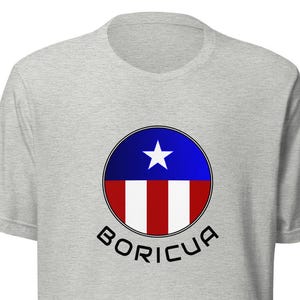 May include: A grey t-shirt with a circular design featuring the Puerto Rican flag and the word "BORICUA" underneath.