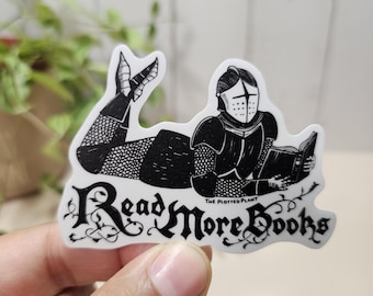 May include: A die-cut sticker featuring a black and white illustration of a knight in full armor lying down and reading a book. The text "Read More Books" is written in a decorative black font below the knight, with "THE PLOTTED PLANT" printed in small letters.