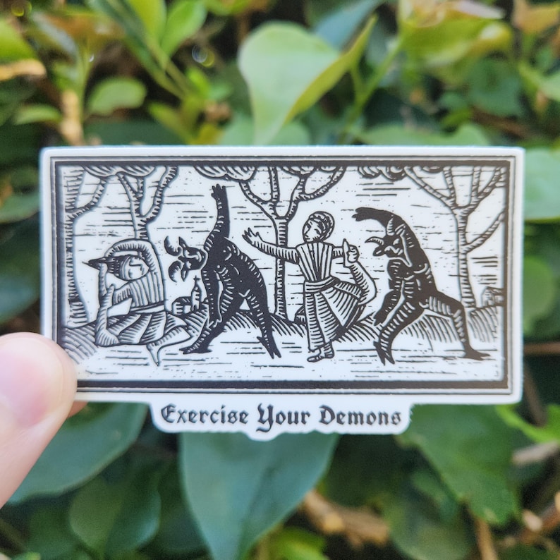 May include: A black and white sticker with a medieval woodcut illustration of figures interacting with demonic creatures in a forest setting. The text "Exercise Your Demons" is at the bottom of the sticker.