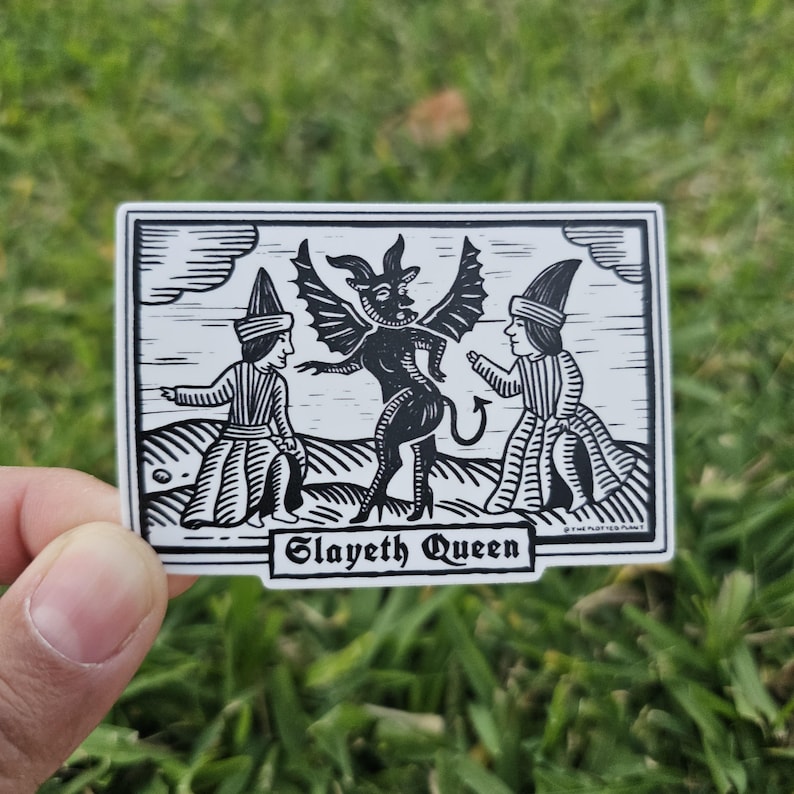 May include: Black and white sticker featuring a stylized illustration of a winged demon and two figures in robes. The text "Slayeth Queen" is displayed in a banner at the bottom of the sticker.