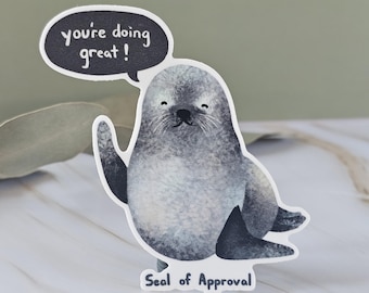 May include: A die-cut sticker featuring a watercolor-style gray seal waving a flipper. A dark gray speech bubble above the seal contains the white text 'you're doing great!' and the text 'Seal of Approval' is printed in white at the bottom.