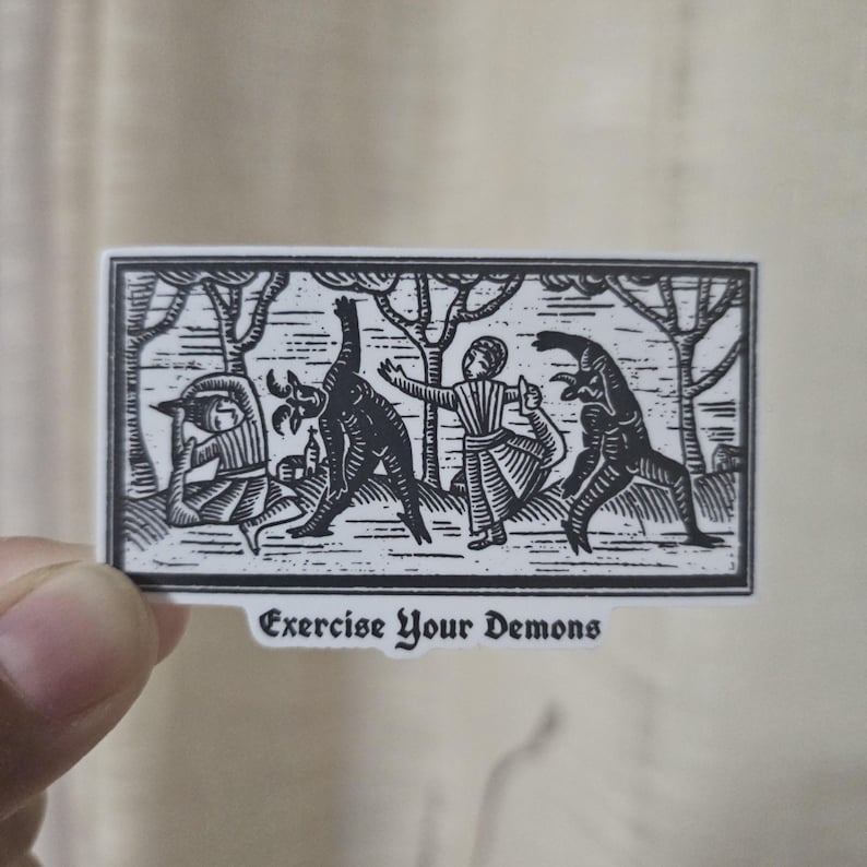 May include: A black and white sticker featuring a stylized illustration of figures interacting with demonic creatures in a forest setting. The text "Exercise Your Demons" is printed at the bottom of the sticker.
