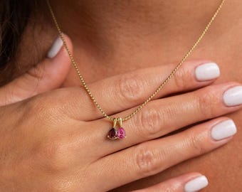 Puede incluir: Un collar de cadena dorada con dos pequeños colgantes en forma de pera. Un colgante es una piedra preciosa de color rojo intenso y el otro es una piedra de color rosa brillante. Ambas piedras están engastadas en metal dorado en la cadena.