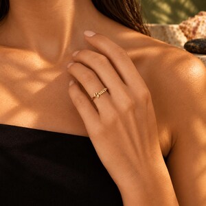 Könnte beinhalten: Ein goldfarbener Ring mit dem Namen Grace in Schreibschrift. Der Ring ist schmal und poliert, wobei das Namensschild mittig auf der Ringschiene sitzt. Das Metall hat eine warme, reflektierende Oberfläche, die das Licht auf den Buchstaben fängt.