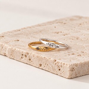 May include: Two thin metal rings, one gold-toned and one silver-toned, each featuring a delicate engraved floral design. The gold ring displays a sunflower motif, while the silver ring shows a sprig of small blossoms, both with a smooth finish.