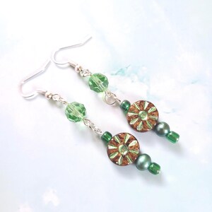 Peut inclure: Boucles d'oreilles pendantes avec crochets argentés, perles vertes facettées et petites perles rondes marron et vertes à motifs floraux. Les boucles d'oreilles ont un aspect délicat et artisanal.