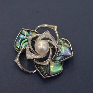 May include: A silver flower brooch with a pearl in the center and abalone shell accents.