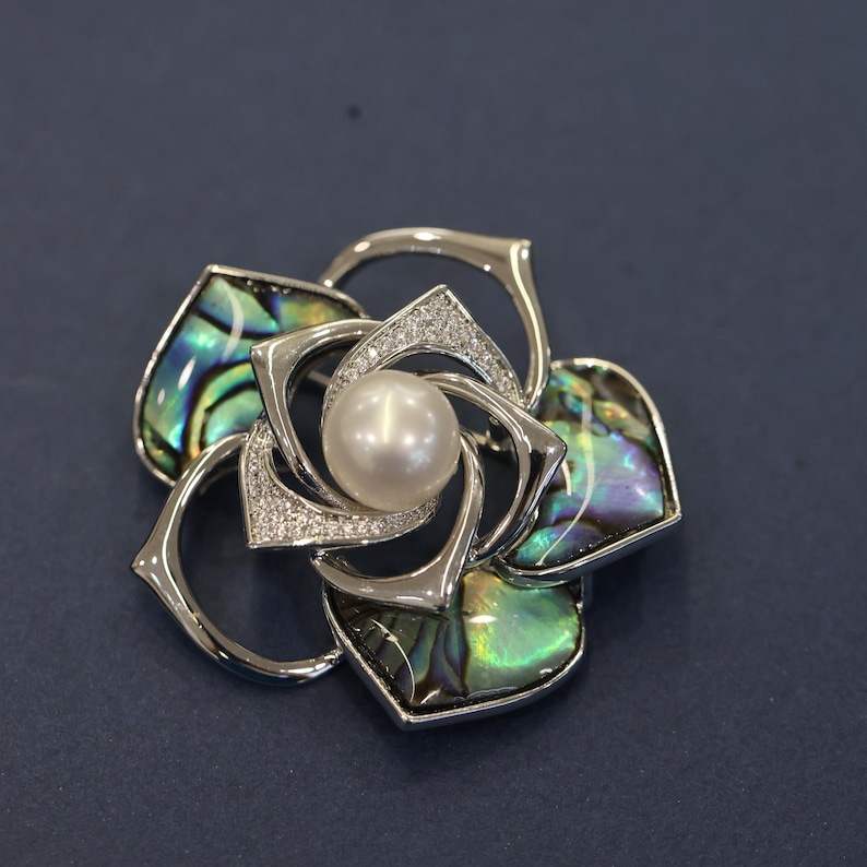 May include: A silver flower brooch with a pearl in the center and abalone shell accents.