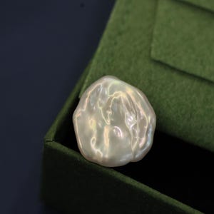 May include: A large, white, baroque pearl with an iridescent sheen. The pearl is irregularly shaped and has a smooth, glossy surface.