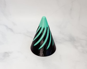 May include: A black and teal cone-shaped ring holder with a swirl design.