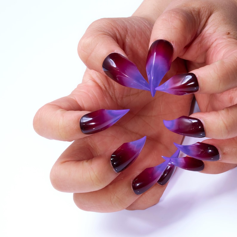 May include: A set of long, pointed, ombre nails with a dark red base and a light purple tip.