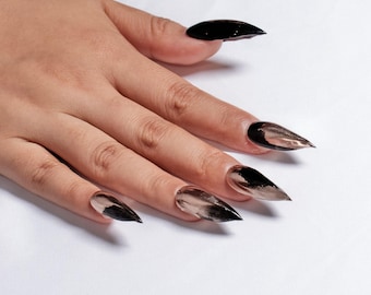May include: A hand with long, black and clear stiletto nails. The nails are painted with a black and clear ombre effect.