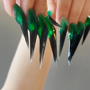 May include: Long, stiletto-shaped artificial nails featuring a translucent emerald green base that transitions into a solid, opaque black tip. The glossy finish creates a sharp, pointed silhouette with a smooth gradient effect across each nail surface.