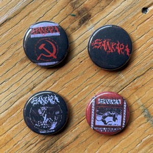 Puede incluir: Cuatro chapas redondas con el nombre del grupo Sankara. Una chapa muestra una hoz y un martillo rojos, otra el nombre del grupo en texto rojo, y dos chapas representan imágenes de tigres con el texto Sankara y otras inscripciones.
