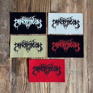 May include: Five rectangular patches with the word "PANOPTICON" in a gothic font. The patches are black, white, olive green, red, and black with red text. The patches are arranged on a wooden surface.
