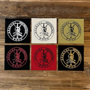 May include: Six square patches with the words "ANARCHY DESTRUCTION" and a graphic of a skull with horns. The patches are in black, white, red, and gold colors. The word "ZOUO" is at the bottom of each patch.