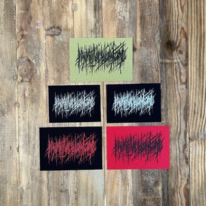 May include: Five rectangular patches in green, black, and red. Each patch features a unique abstract design in contrasting colours. The patches are arranged on a wooden surface.