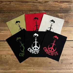 May include: A collection of fabric patches in various colors, including black, red, and beige, each featuring a stylized crucifix design. Some patches have the word "CRUCIFIX" printed in a contrasting color.