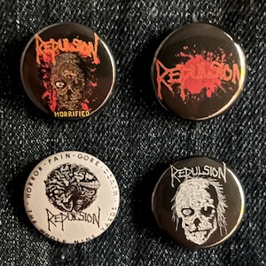 May include: Four round Repulsion band buttons. Two buttons have a black background with red text and graphics. One button has a white background with black text and graphics. The fourth button has a black background with white text and graphics.