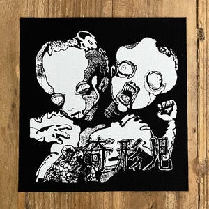 May include: Black and white patch featuring a grotesque illustration of two figures with distorted features and large eyes. The figures are set against a black background, with Japanese characters at the bottom.