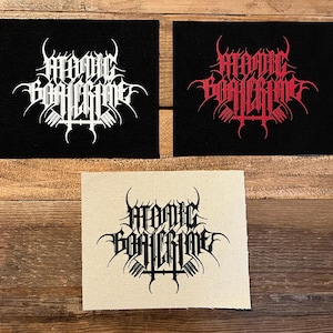 Pode incluir: Três patches quadrados com o texto "ATOMIC BOMBGRIME" em uma fonte gótica. Dois patches são pretos com texto branco e vermelho, e um é bege com texto preto. Os patches são provavelmente para roupas.