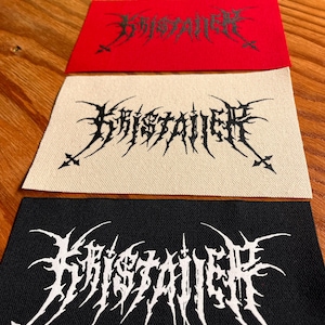 Może przedstawiać: Cztery prostokątne naszywki z tkaniny z napisem KRISTALLER wykonanym stylizowaną, poszarpaną czcionką typu black metal. Naszywki występują w kolorze oliwkowym, czerwonym, złamanej bieli i czarnym, z nadrukiem w kontrastującym kolorze na każdej.